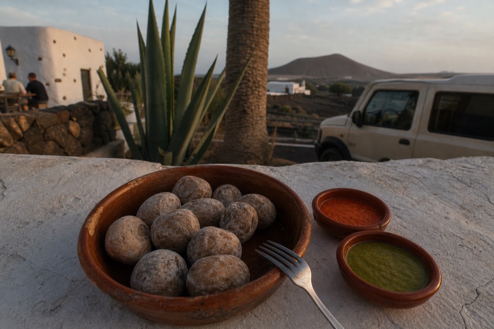 Small wrinkled potatoes in a clay dish with bowls of red and green mojo sauce