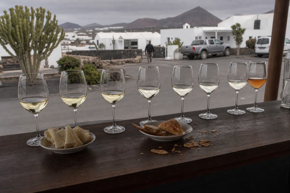 A row of white wine glasses and a glass of amber sweet wine beside small plates of cheese and honeyed pastry