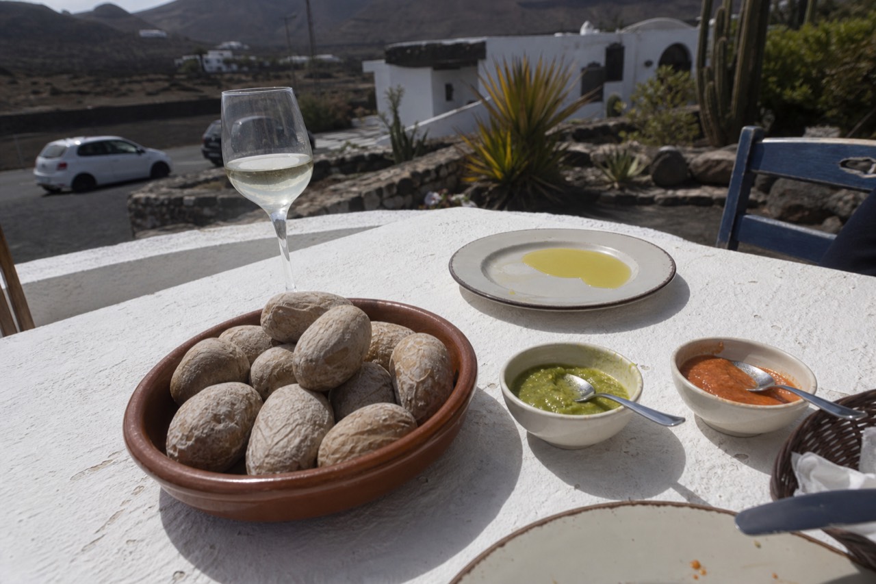 A table of wrinkled potatoes with red and green mojo sauces and a glass of white wine