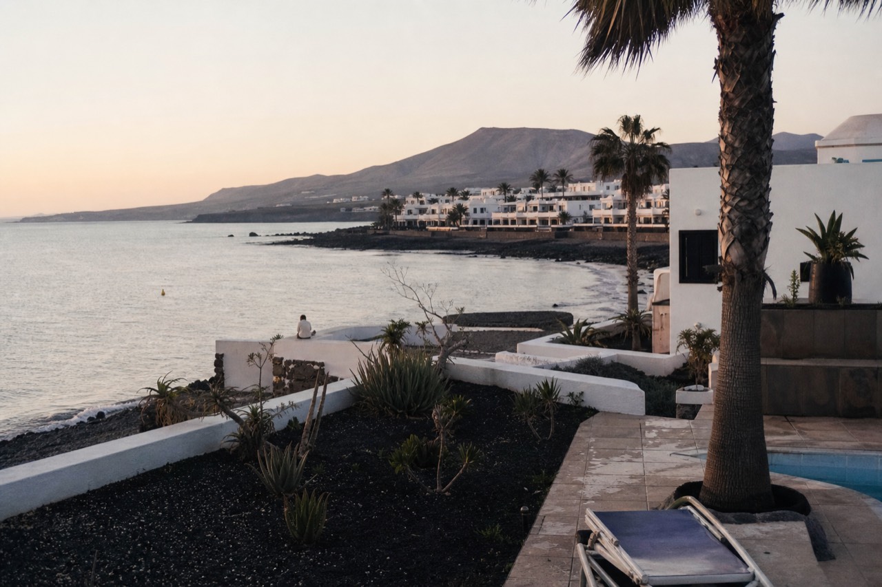 A low white Lanzarote resort building beside a calm bay at golden hour