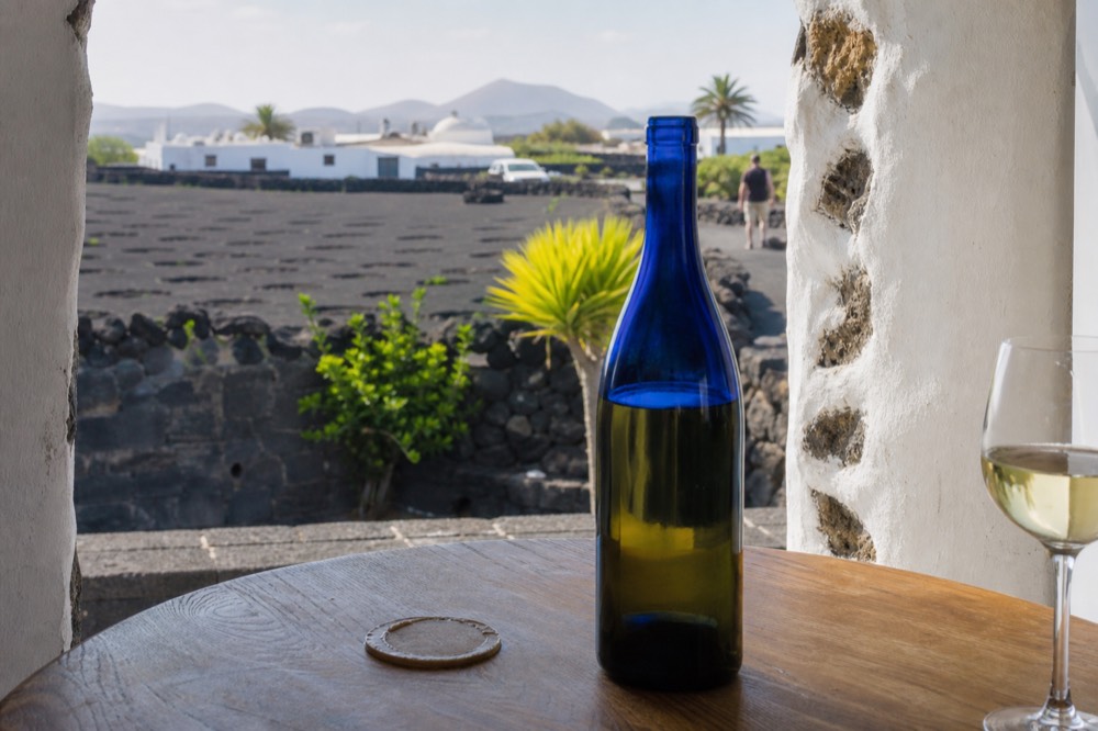 A blue glass wine bottle on a tasting table with volcanic ash and stone vine walls behind it