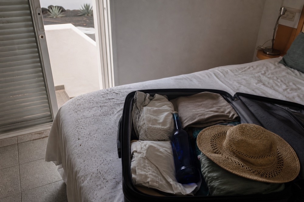 A blue wine bottle packed in a suitcase beside holiday clothes