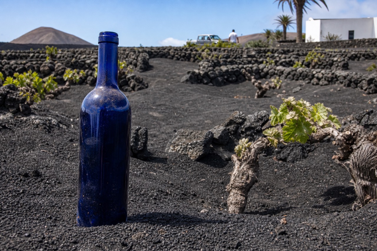 A dry white wine in a distinctive blue bottle standing among black volcanic ash and vine pits in La Geria
