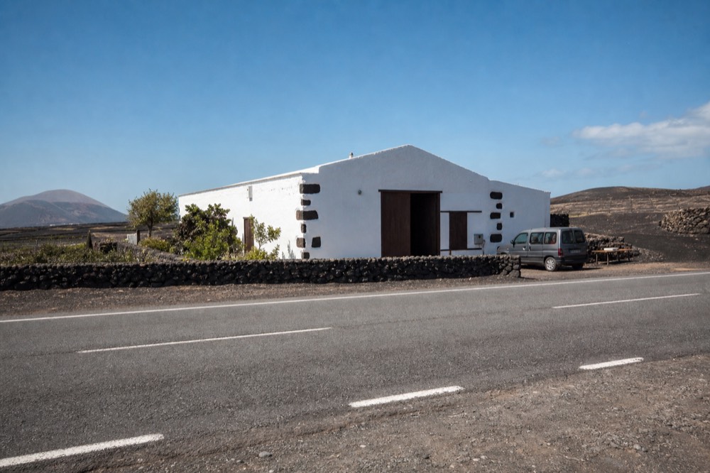 Whitewashed winery building on the LZ-30 road with black ash fields and vine pits beyond