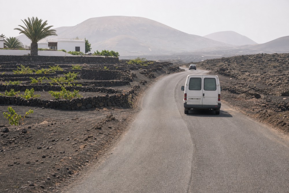 Winding road through black volcanic ash fields with vine pits on both sides