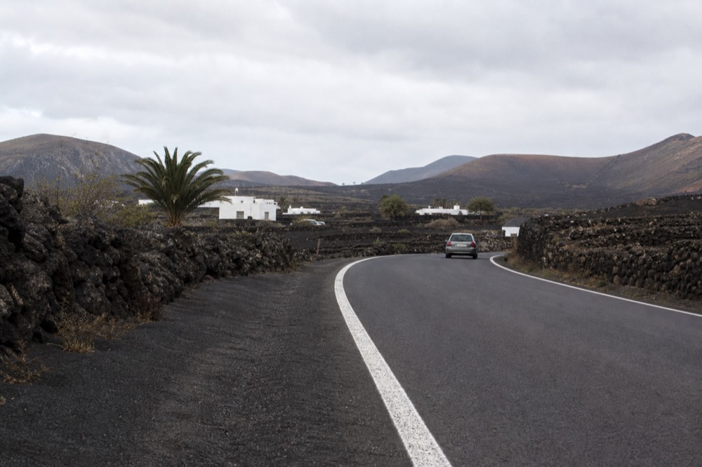 Fresh asphalt on a two-lane road with new white markings curving between black ash slopes