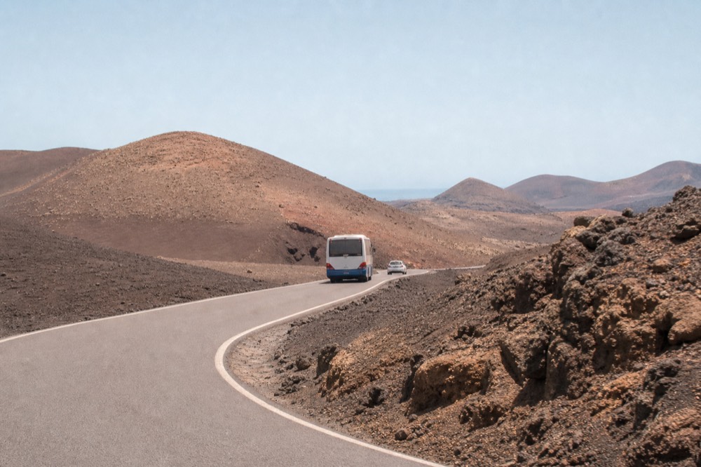 A coach road winding through rust-red and black volcanic slopes inside Timanfaya National Park