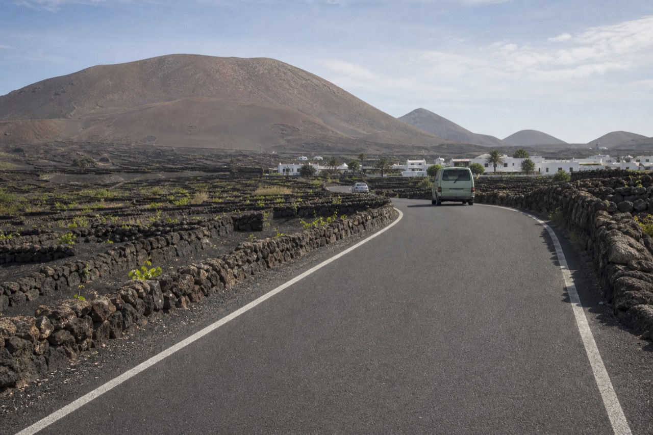 The LZ-30 road winding between black volcanic ash fields and semicircular stone vine walls in La Geria, Lanzarote