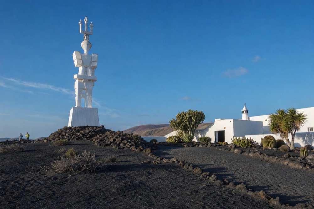 A white monumental sculpture on a volcanic plain beside a museum building