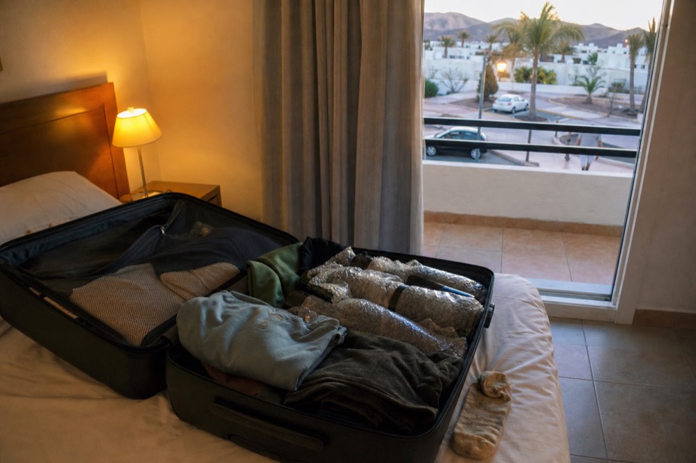 Suitcase open on a hotel bed with wine bottles wrapped in bubble wrap between folded clothes