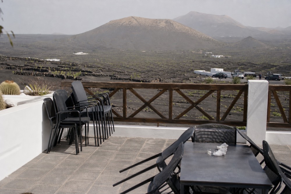 A winery terrace with empty tables overlooking black ash vineyards and distant volcanoes