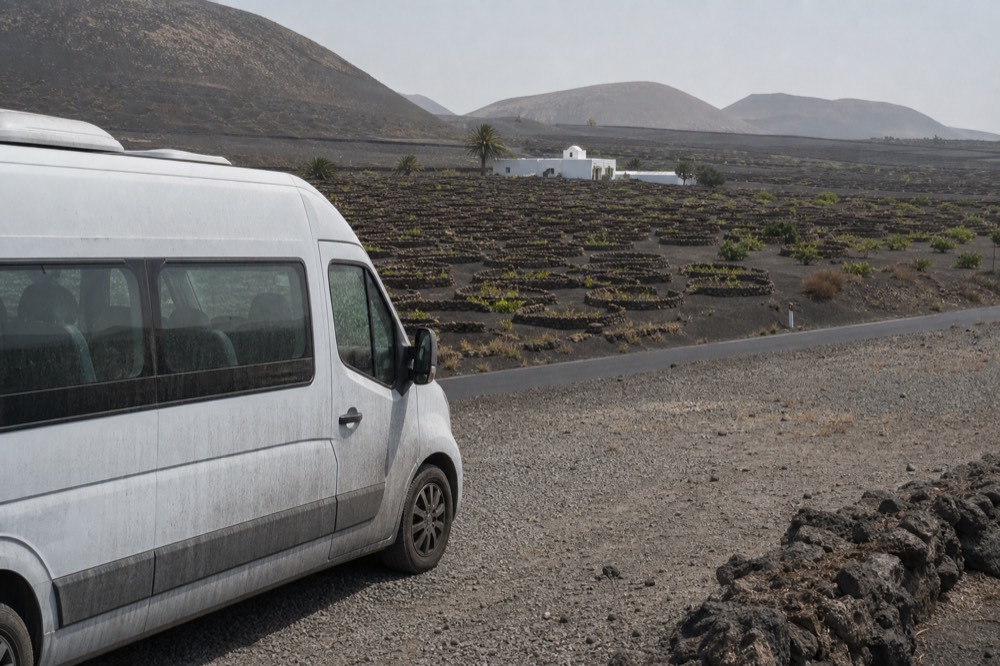 Small minibus parked on a volcanic road beside vine pits